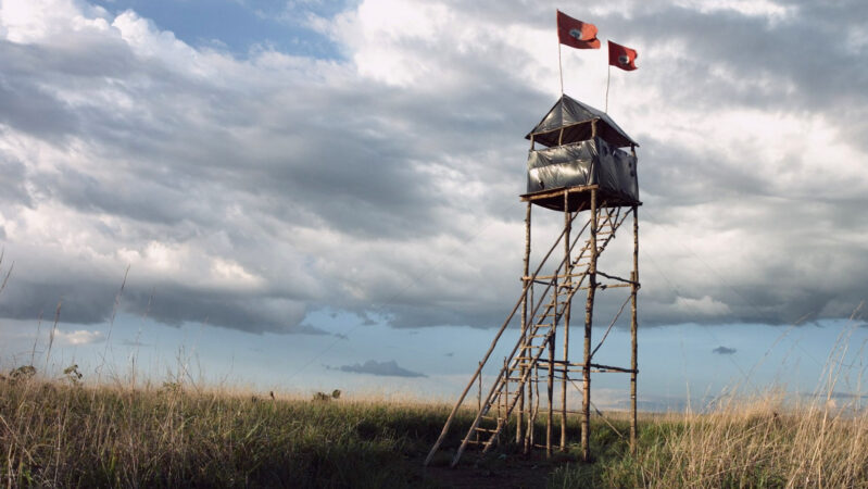 무토지 스틸컷1. 푸른 하늘을 배경으로 둔 광활한 밭에 매우 높은 망루가 세워져 있다. 망루 위에는 무토지농촌노동자운동의 깃발이 바람에 날리고 있다.