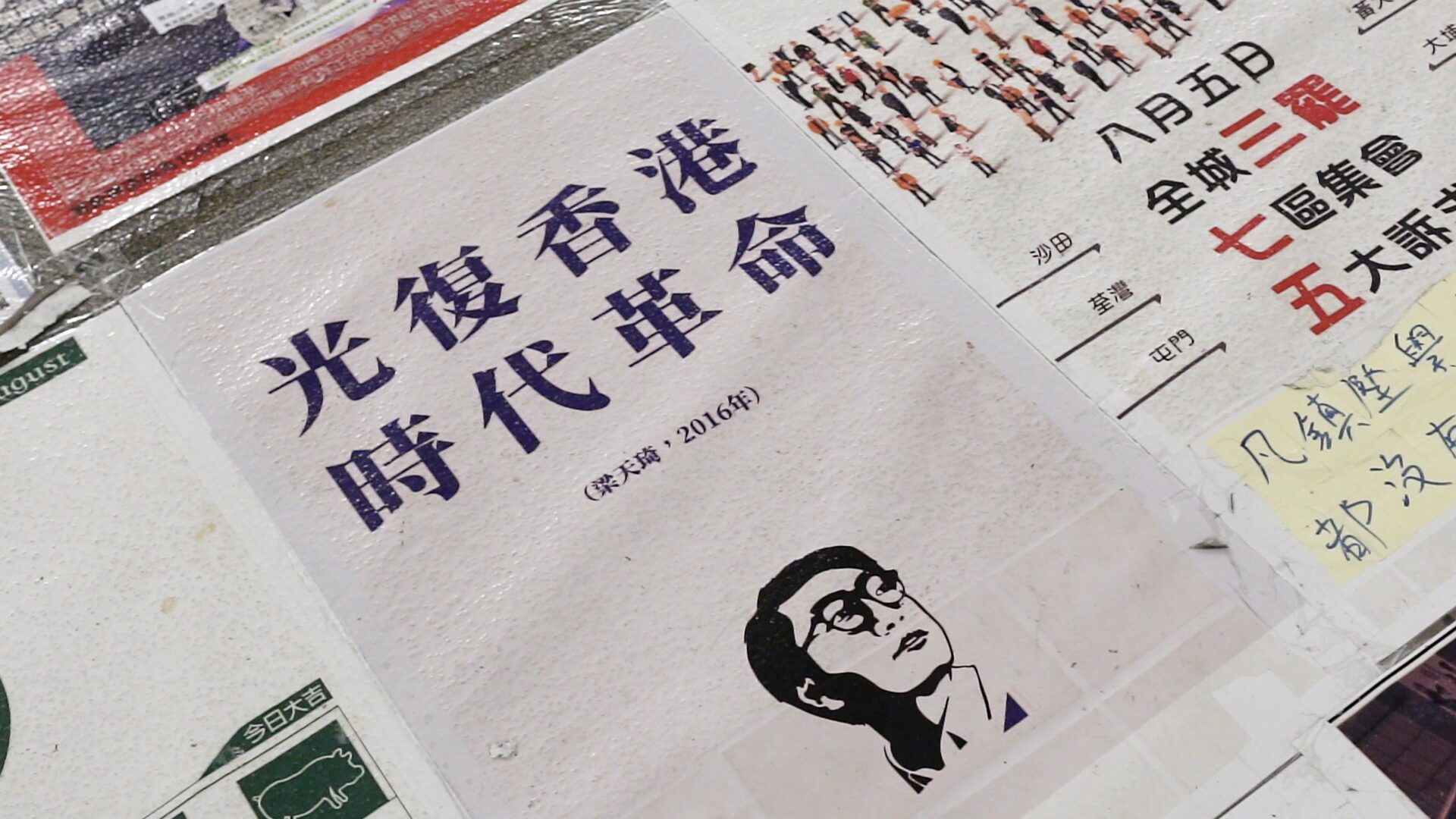 검은 자형화 스틸컷1. 파란색 한자로 ‘광복홍콩 시대혁명’ 이라고 쓰여있는 인쇄물. 주변에는 다른 인쇄물들이 붙어 있다.