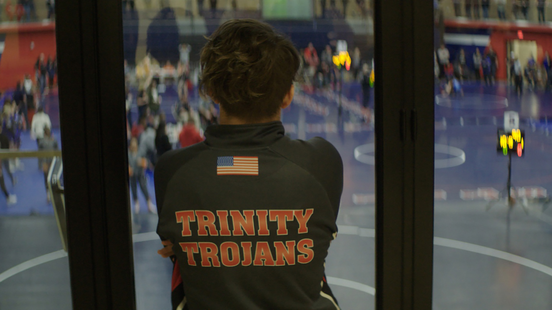게임의 규칙 스틸컷2.성조기와 Triniy Trojans라는 문구가 있는 체육복을 입은 맥의 뒷모습. 맥은 관중들로 가득한 실내 체육관을 내려다보고 있다.