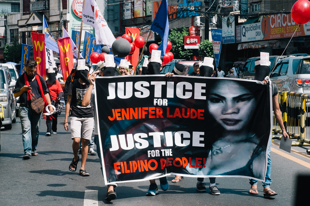 혐오의 시대 스틸컷1.시위대가 간다의 사진과 ‘Justice for Jennifer lauede’라는문구가 있는 플래카드를 들고 거리에서 행진중이다. 시위대는 얼굴을 가리기 위해 복면을 썼고, 몇몇 사람들은 깃발을 들고 있다.