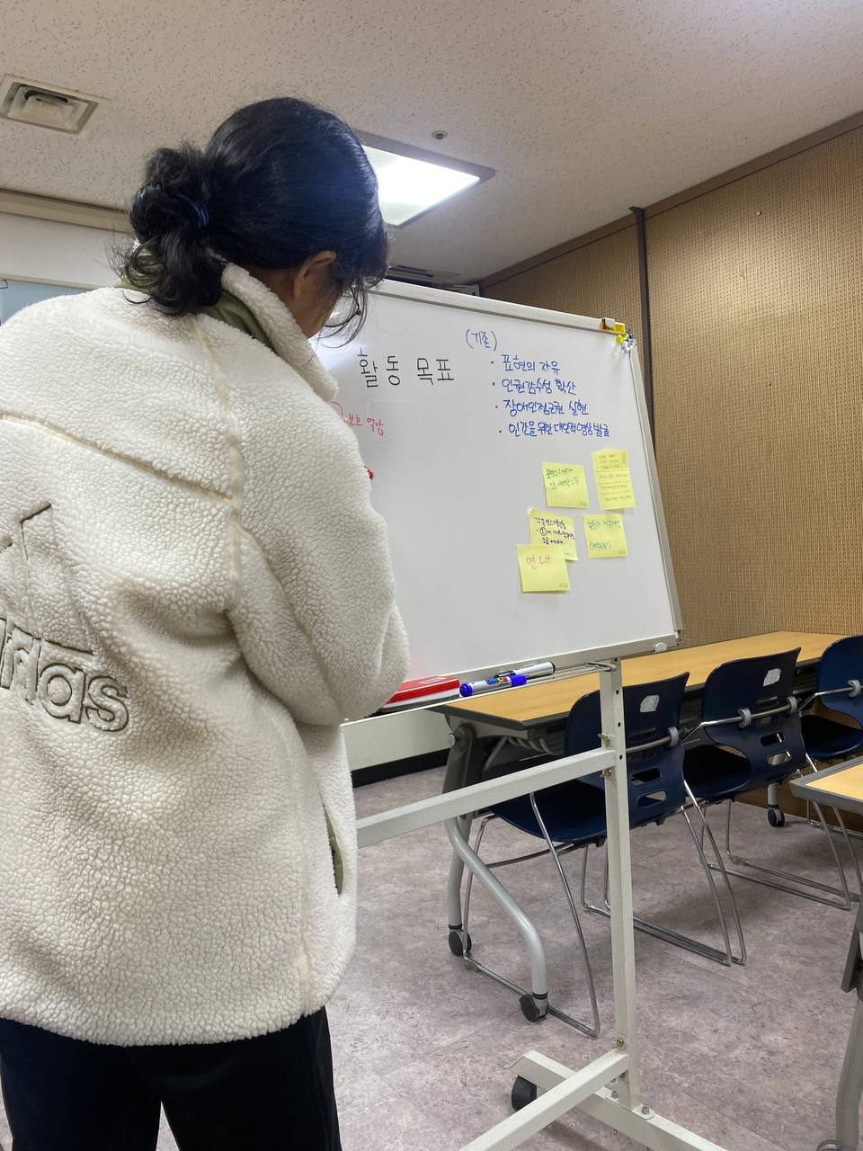 사진. 화이트보드 앞에 선 나기가 글자를 적고 있다. 보드에는 서울인권영화제의 활동목표가 적혀있고 의견이 적힌 포스트잇이 붙어있다.