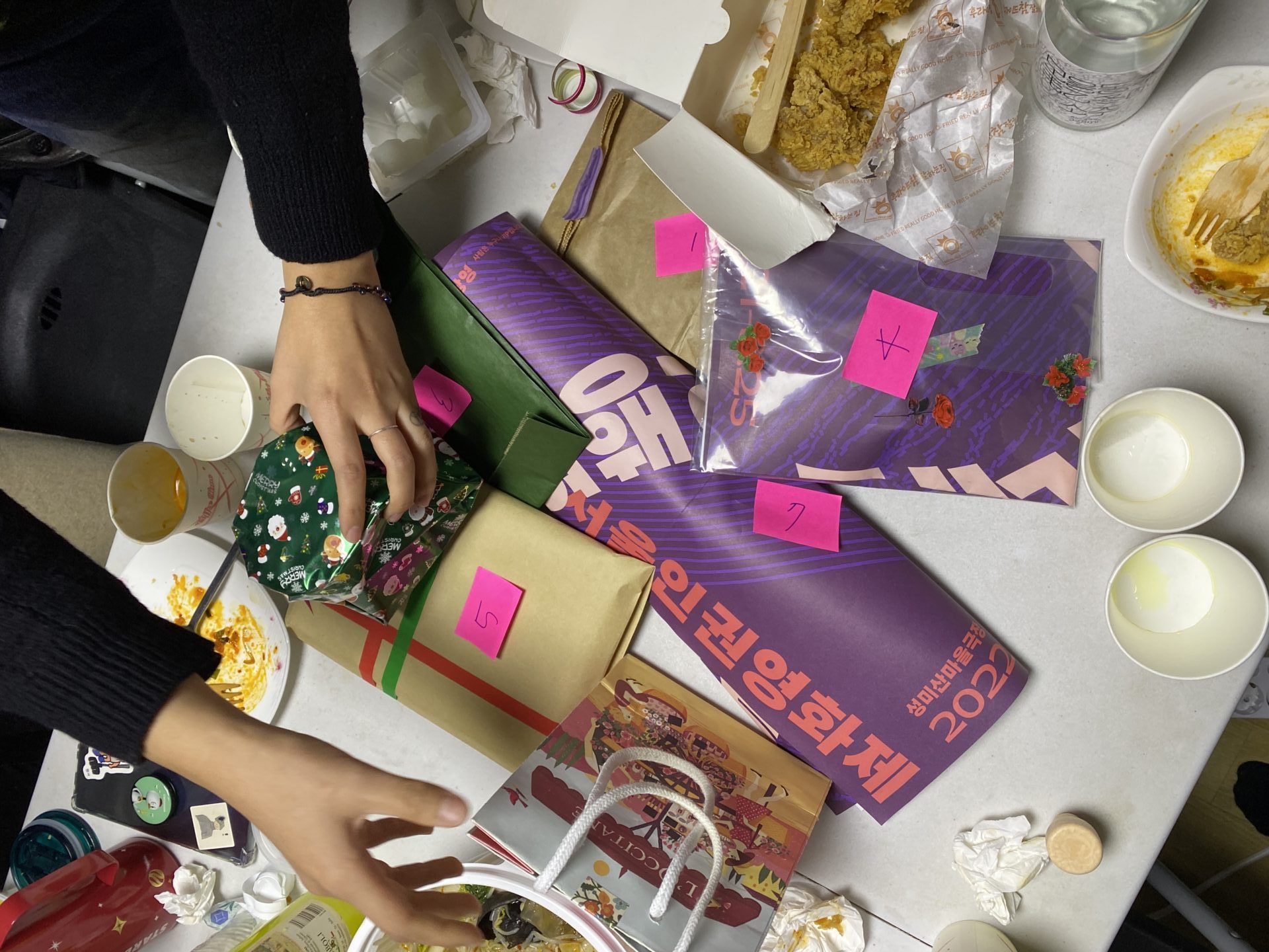 사진1. 간식과 술, 종이컵이 놓인 책상 가운데 각기 다른 크기와 모습으로 포장된 선물들이 1번부터 7번까지의 번호를 달고 놓여 있다. 누군가의 손이 선물들을 정리하고 있다.