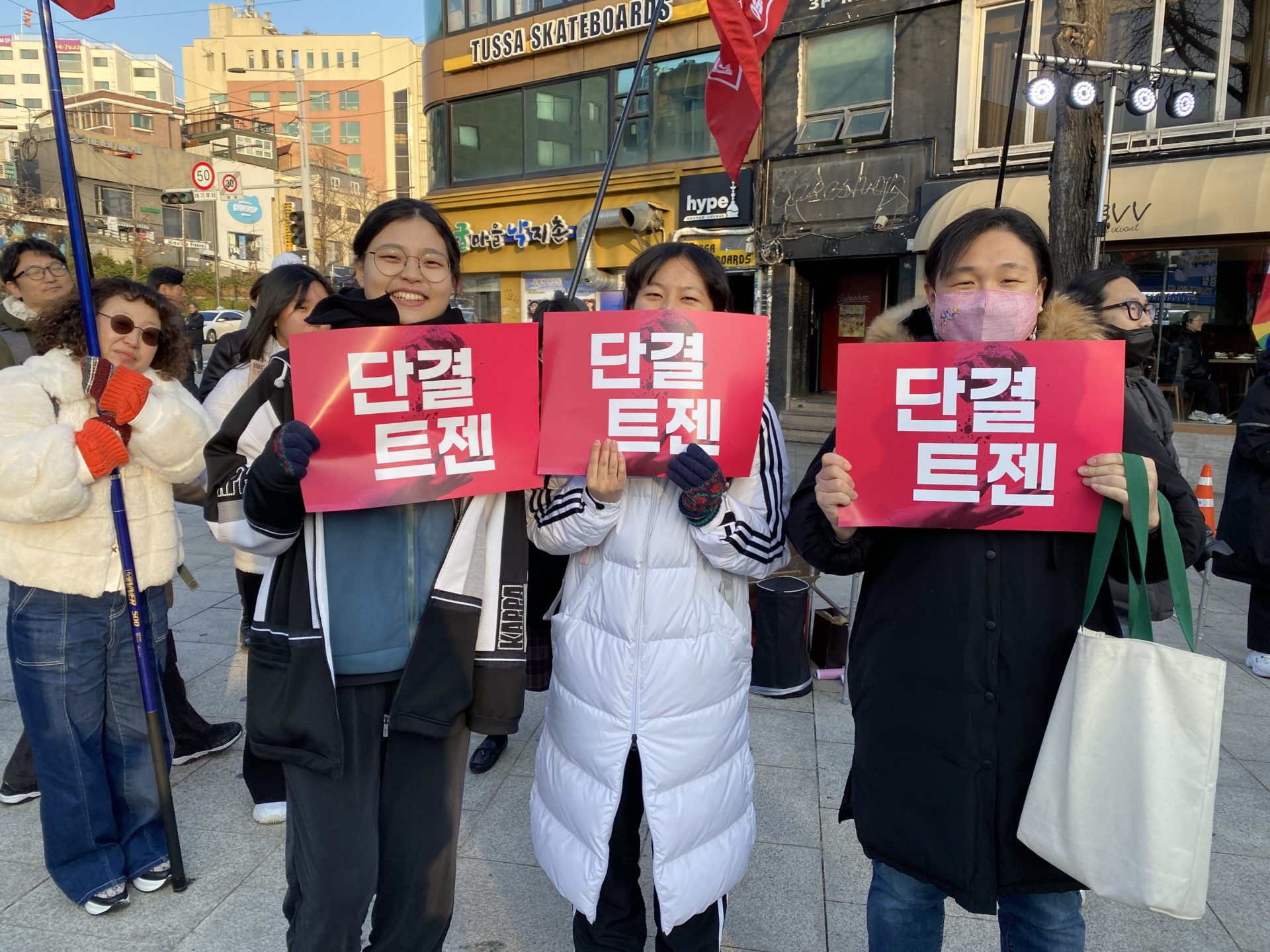 사진1. 광장에 모인 서울인권영화제 자원활동가 나기, 요다, 소하가 '단결 트젠' 피켓을 들고 웃고 있다.