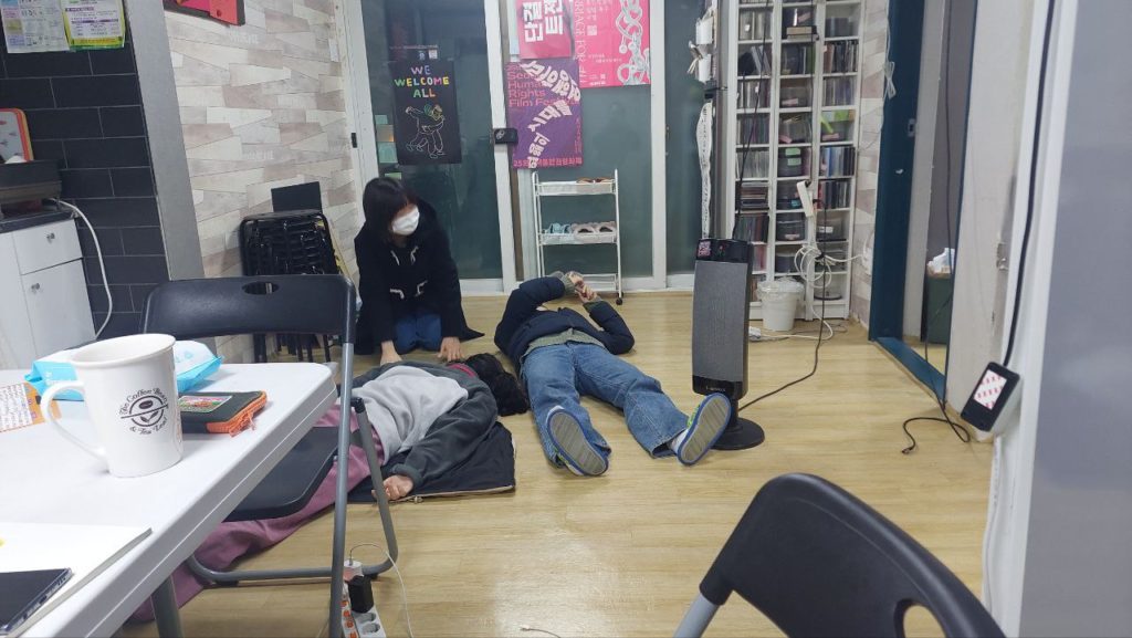 사진2. 서울인권영화제 사무실 마루. 활동가 나기, 고운이 누워있고 마주는 무릎을 꿇고 앉아 있다.