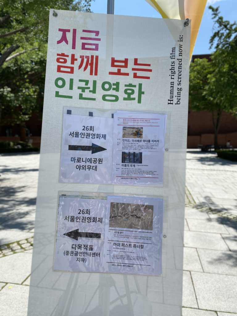 서울인권영화제 엑스배너. 현재 상영 중인 영화 정보가 붙어있다. 마로니에공원 야외무대에서는 <언허드: 마샤페르 야타를 지켜라>,<이름의 무게>가 상영 중이고 다목적홀에서는 <My First Funeral>이 상영중이라고 써있다.