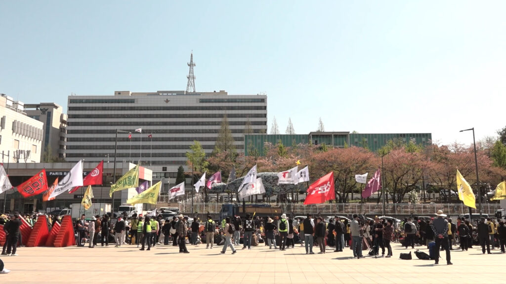 스틸 사진. 깃발을 들고 거리를 행진하는 대오.