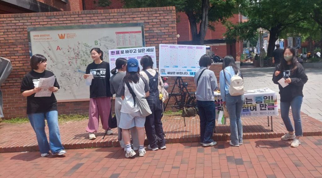 사진. 안나, 나기, 마주, 고운이 마로니에 공원 앞에서 길거리 캠페인을 진행하고 있다. 4명의 행인이 길거리 캠페인에 참여하고있다.