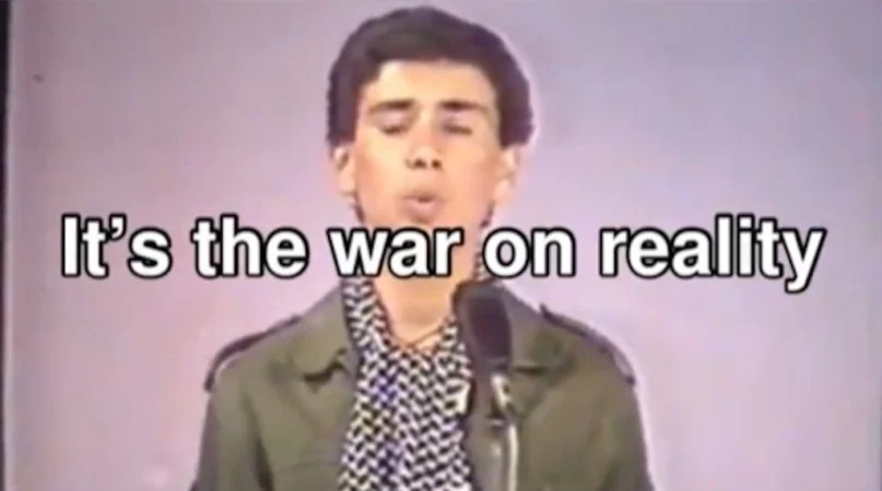 스틸컷. 인터넷 영상 캡처 화면. "It's the war on reality"라는 텍스트 뒤에 말하고 있는 사람이 있다.
