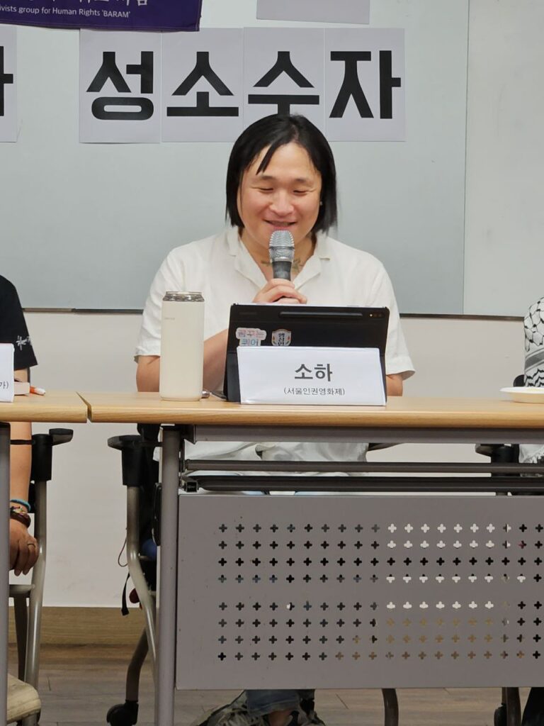 사진. 소하가 프라이드 수다회 패널 자리에 앉아있다. 마이크를 잡고 웃으면서 이야기하고 있다.