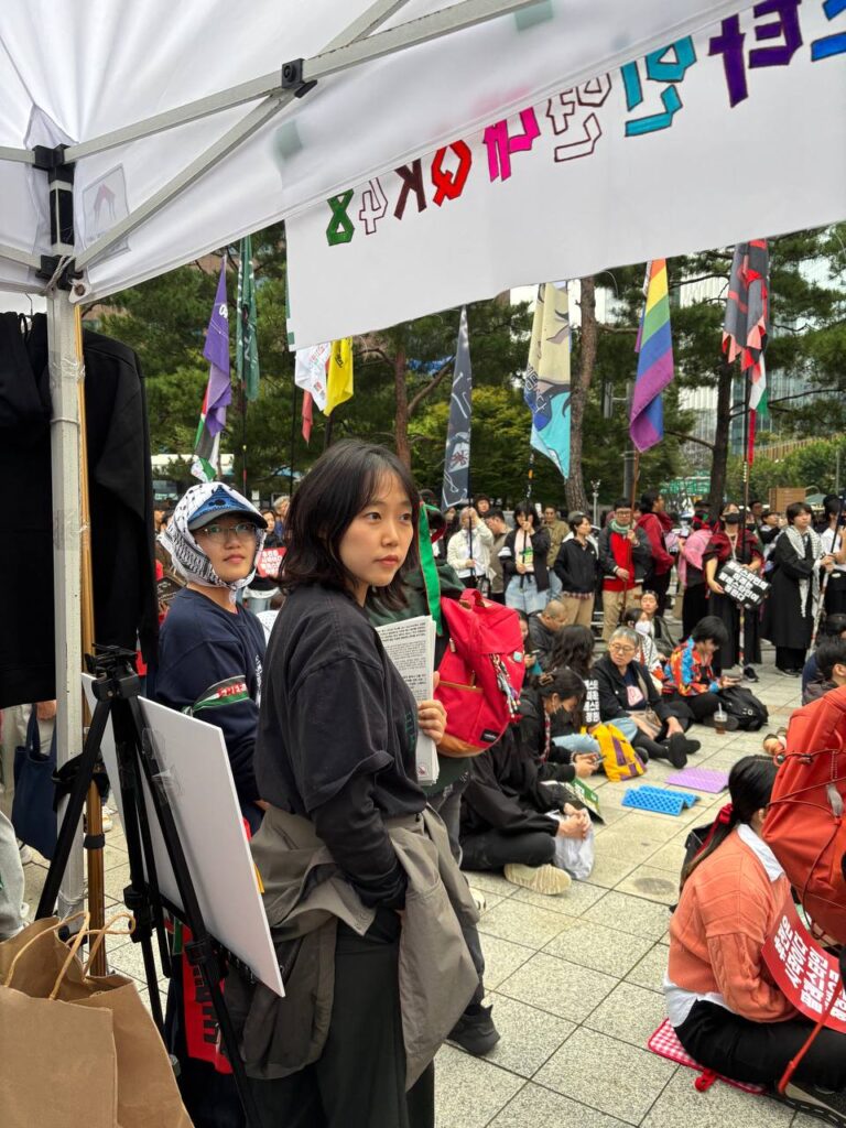사진2. QK48 부스 앞에서 서울인권영화제 고운 활동가, 제주퀴어프라이드 도윤 활동가가 FAQ 신문을 들고 서 있다.
