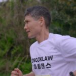 스틸컷1. 김동수(흰색 반팔티를 입고 짧게 깎은 머리를 한 중년)가 달리고 있다. 초록 풀이 가득하다.