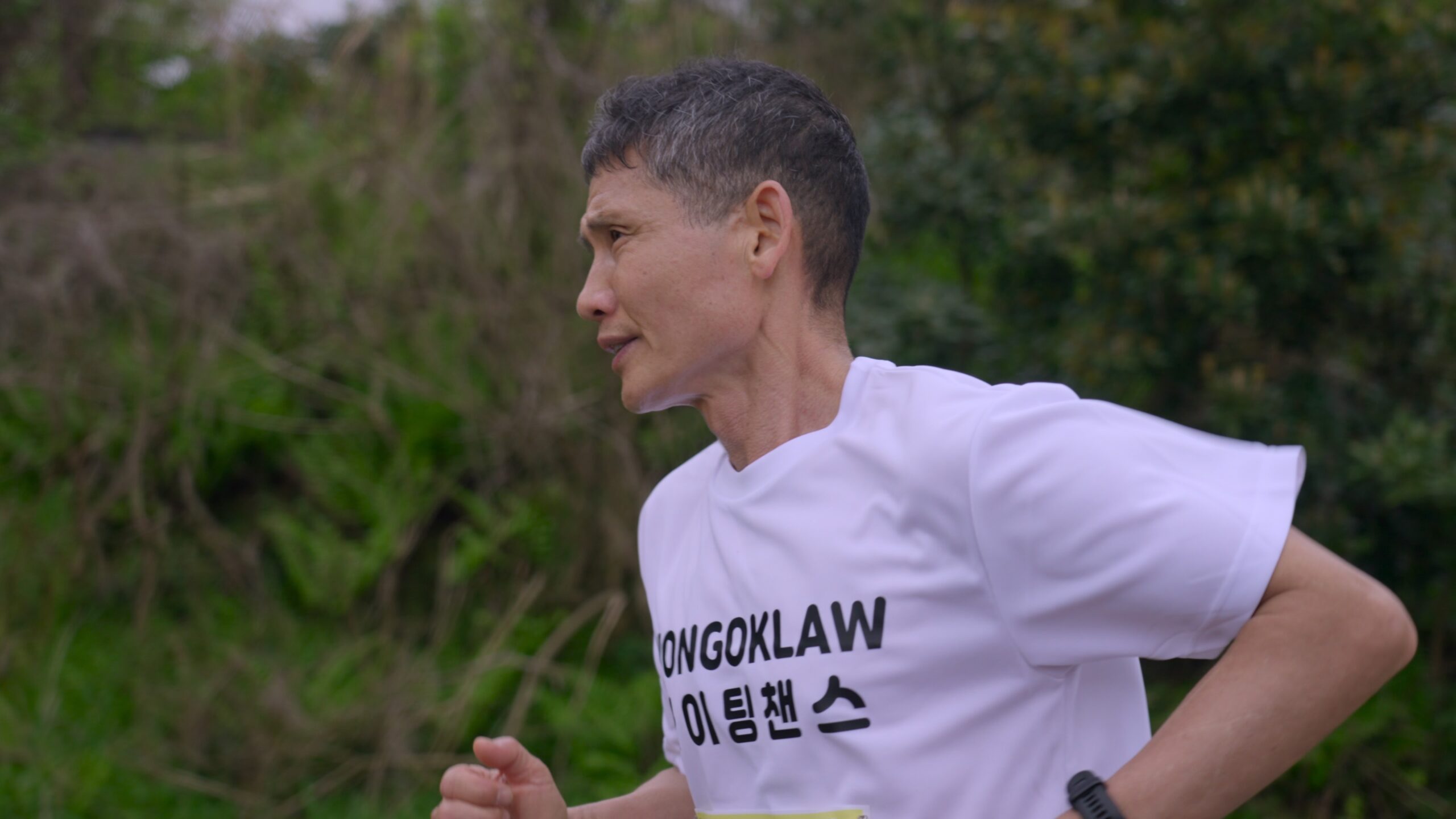 스틸컷1. 김동수(흰색 반팔티를 입고 짧게 깎은 머리를 한 중년)가 달리고 있다. 초록 풀이 가득하다.