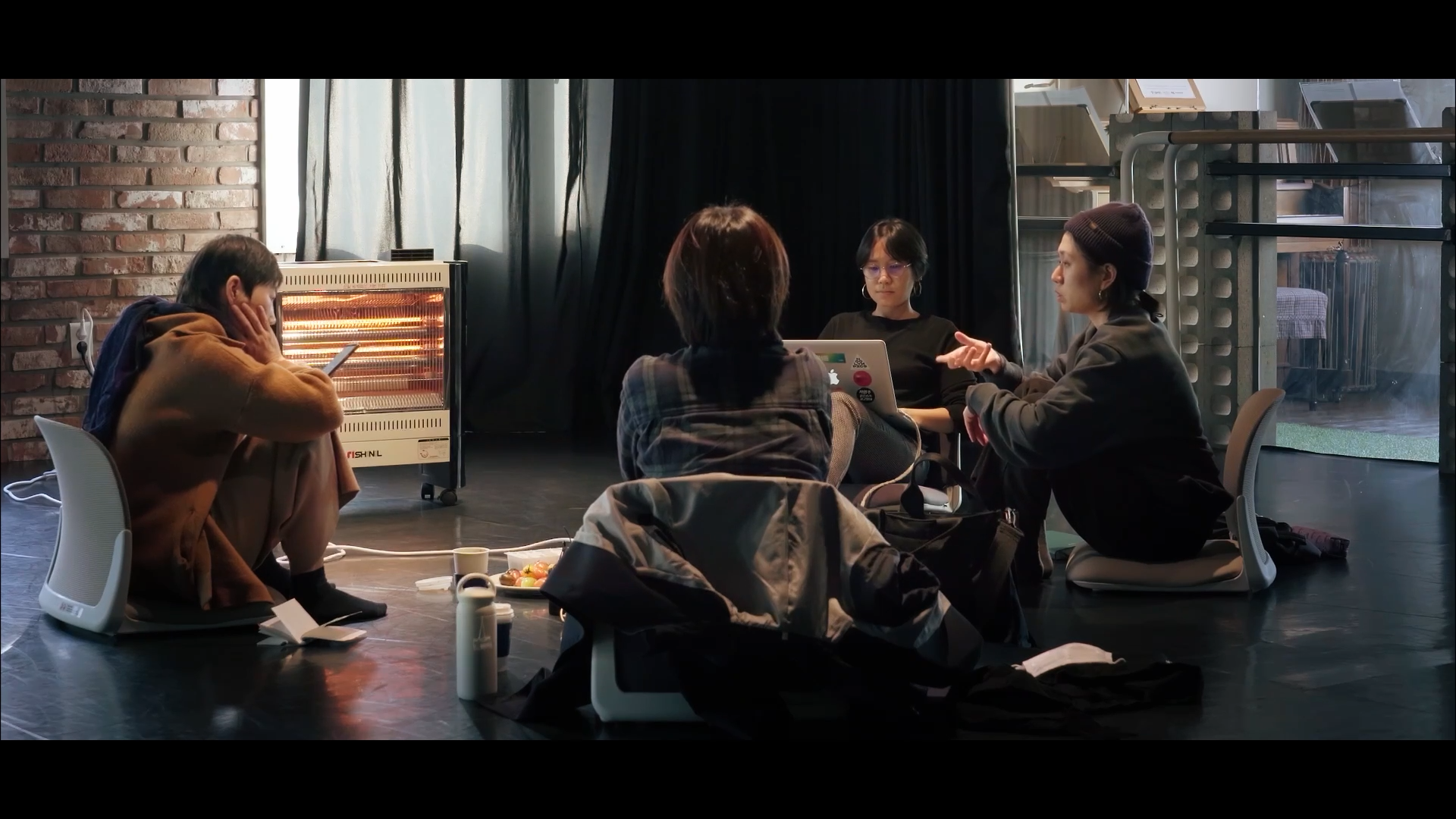 스틸컷3. 밝은 낮, 연습실 바닥에 네 사람이 마주 앉아 회의를 하고 있다.