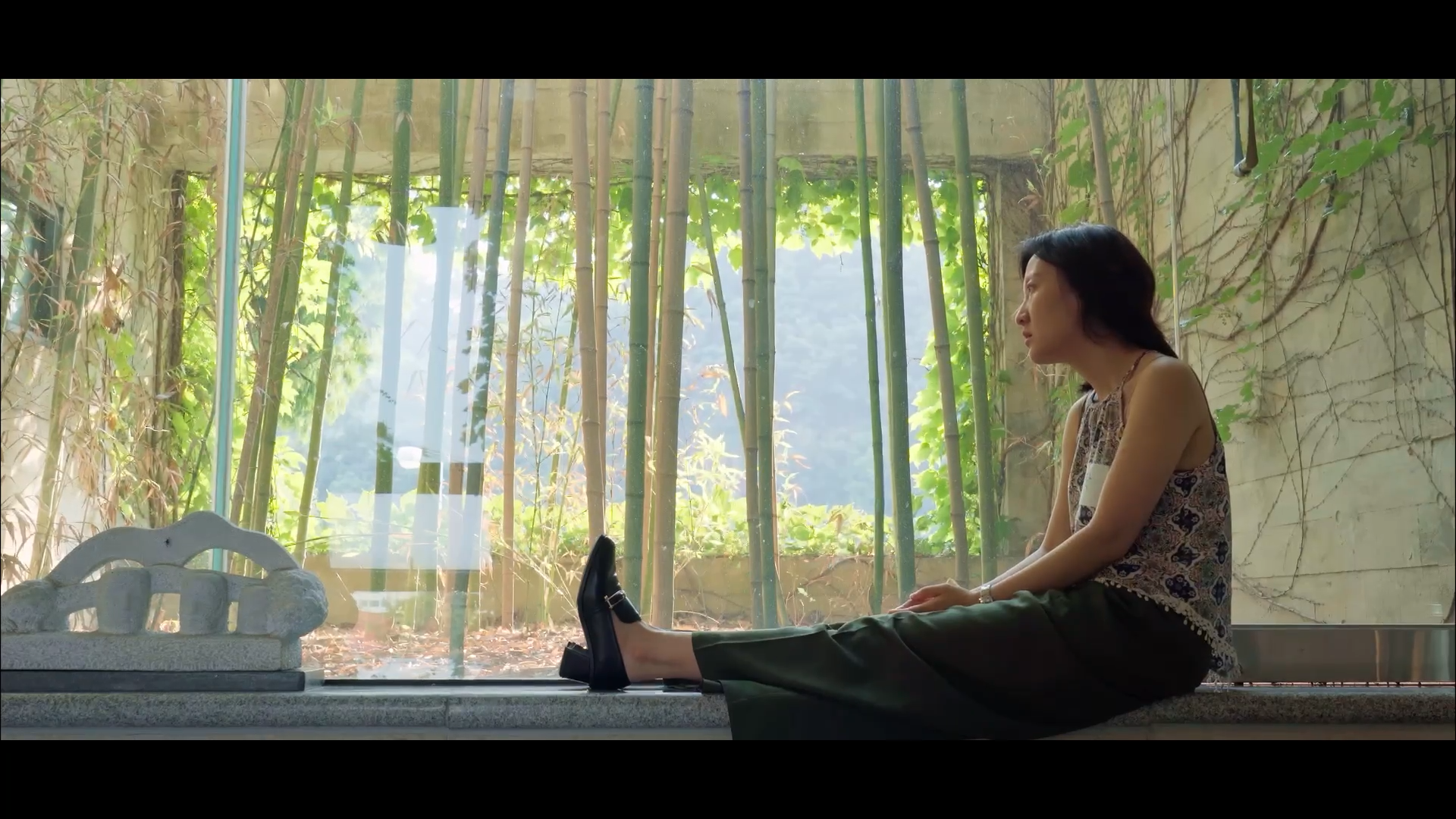 스틸컷4. 밝은 낮, 유리창 앞. 검은 긴 머리의 사람이 정면을 바라보며 대리석 다리를 뻗은 채 앉아있다.