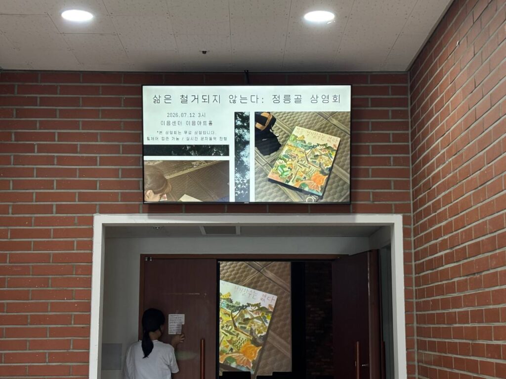 사진1. 상영회 공간인 이음아트홀 입구 위 모니터에 상영회 포스터. 입구 문에 안내문을 붙이는 활동가.